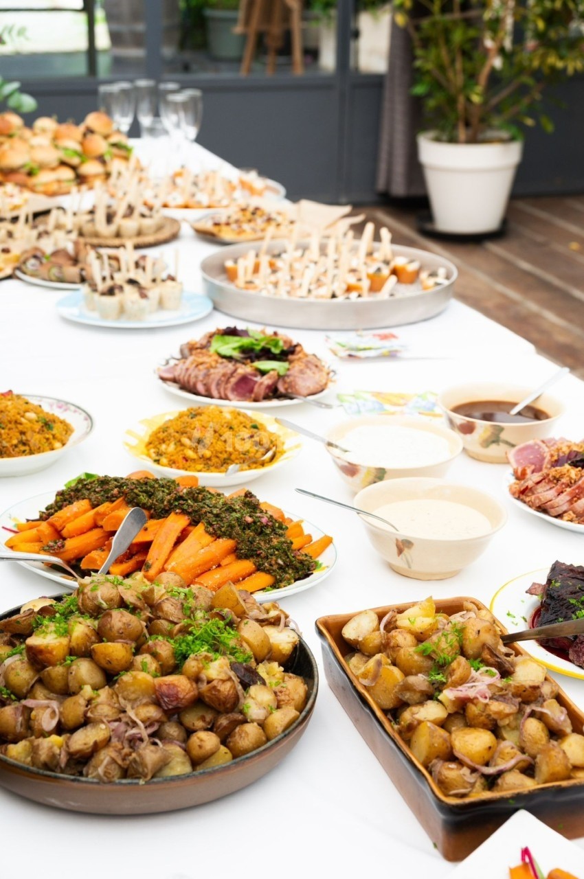 Buffet varié avec plats de légumes, pommes de terre, sauces et viandes disposés sur une table blanche.