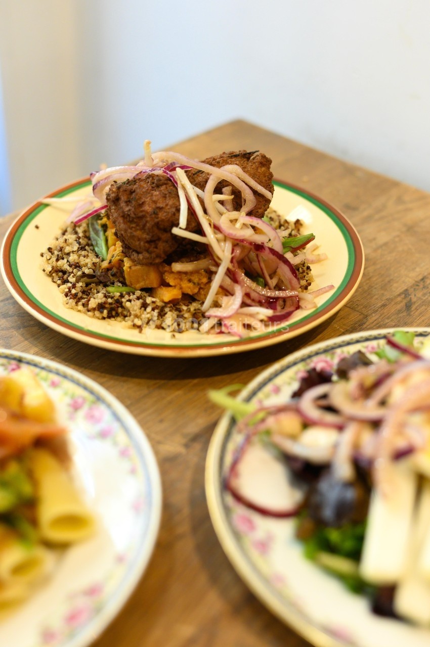 Assiette de viande servie sur un lit de quinoa avec légumes et oignons rouges, posée sur une table en bois.