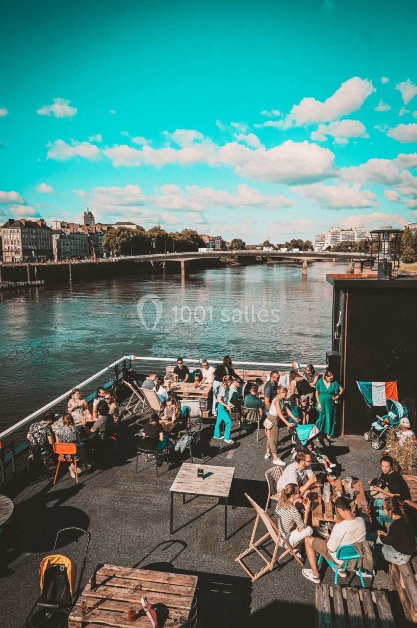 Personnes assises et debout sur une terrasse au bord d'une rivière, par une journée ensoleillée.