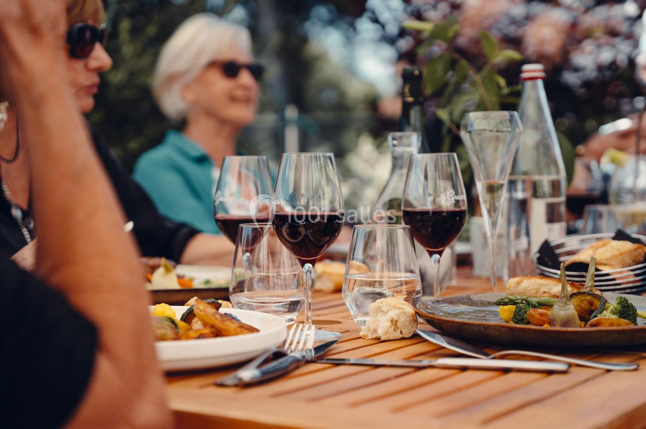 Repas convivial en extérieur avec des verres de vin rouge, des assiettes de nourriture et des convives autour d'une table en…