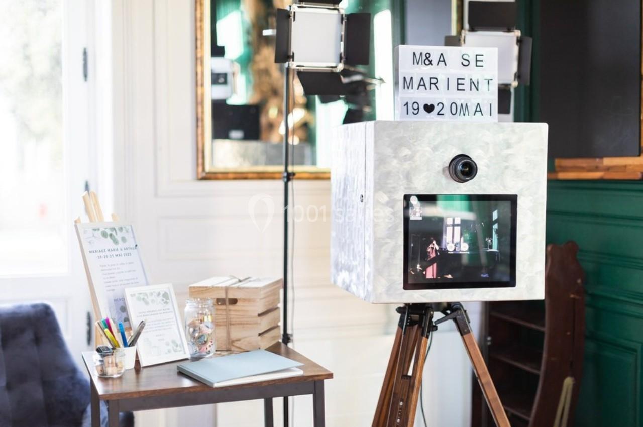 Borne photo rétro sur trépied avec écran et panneau lumineux, entourée de décorations et accessoires de mariage.