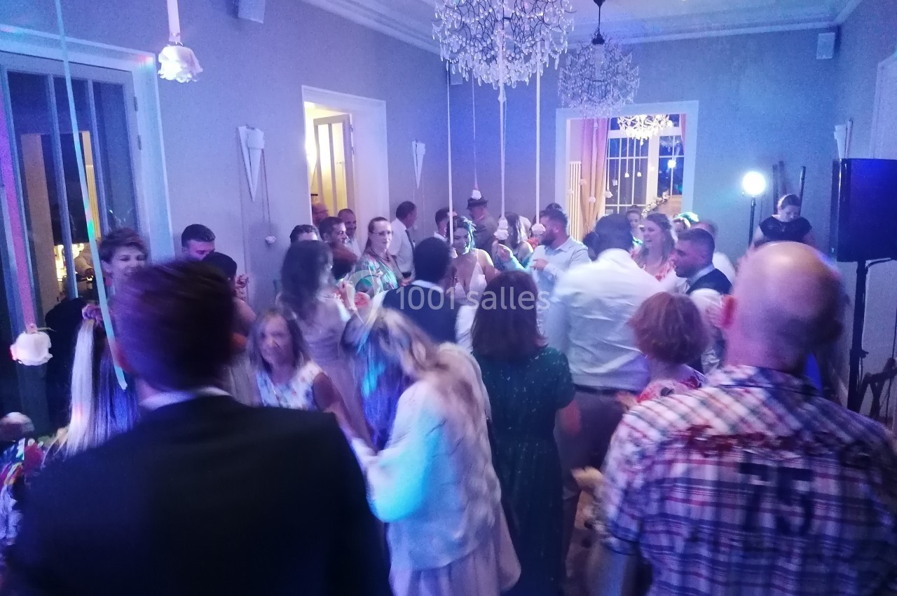 Groupe de personnes dans une salle éclairée, dansant et discutant lors d'un événement festif.