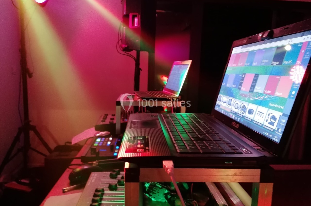 Poste de DJ avec ordinateurs portables, table de mixage et éclairage coloré dans une ambiance de soirée.