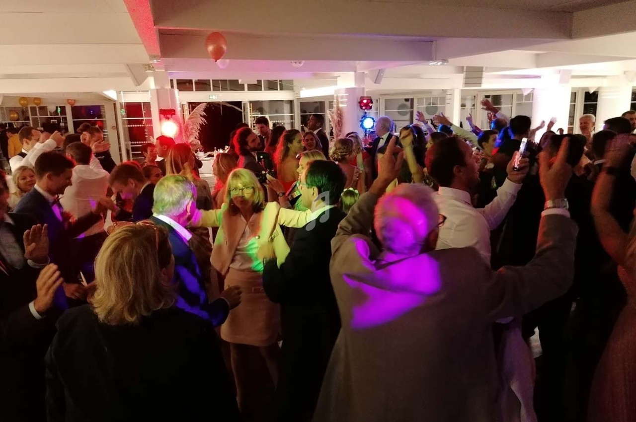 Groupe de personnes dansant dans une salle éclairée par des lumières colorées lors d'une fête ou d'un événement.