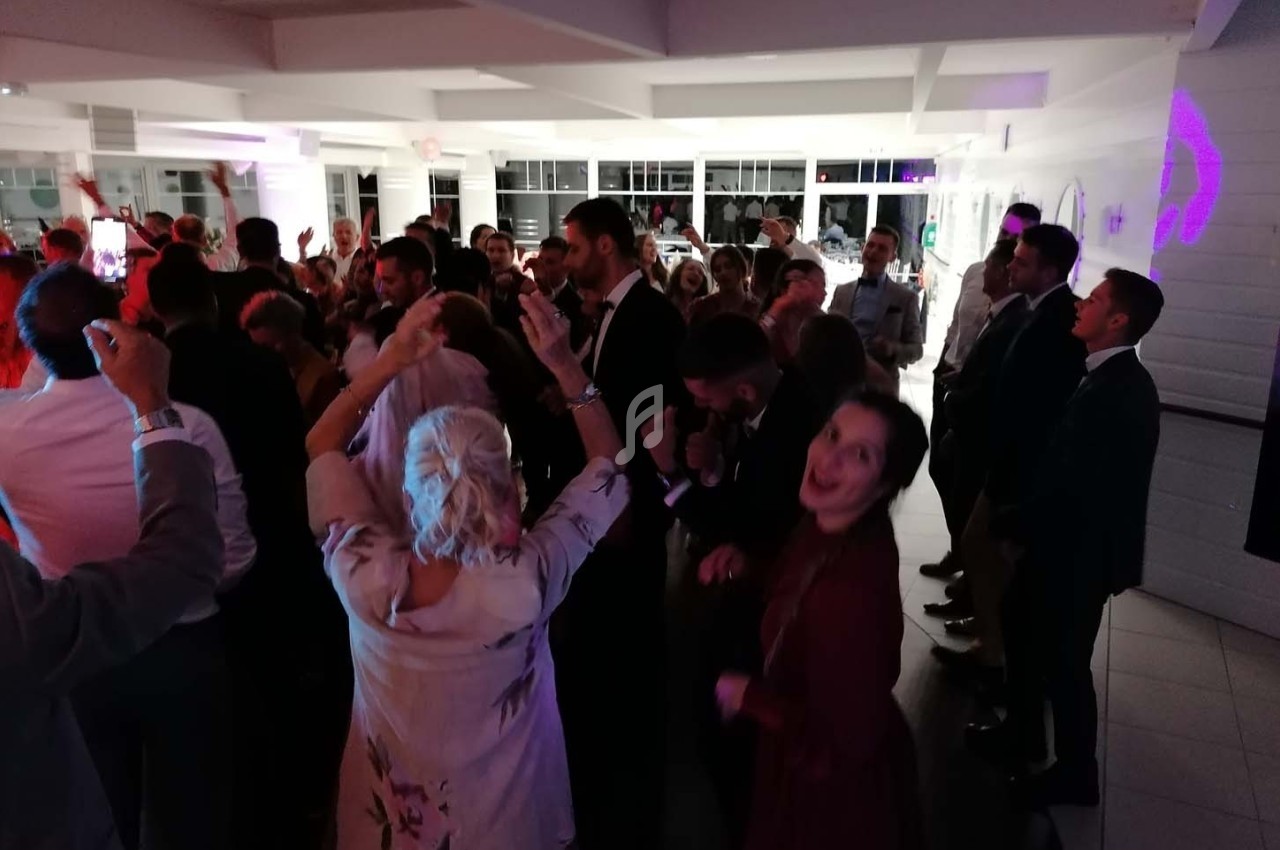 Groupe de personnes dansant et célébrant dans une salle éclairée, ambiance festive en soirée.