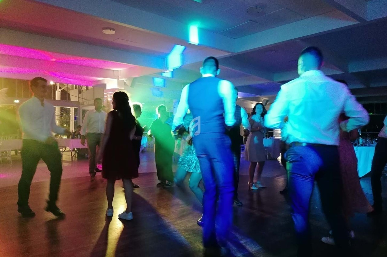 Des personnes dansent sur une piste éclairée par des lumières colorées dans une salle de réception.