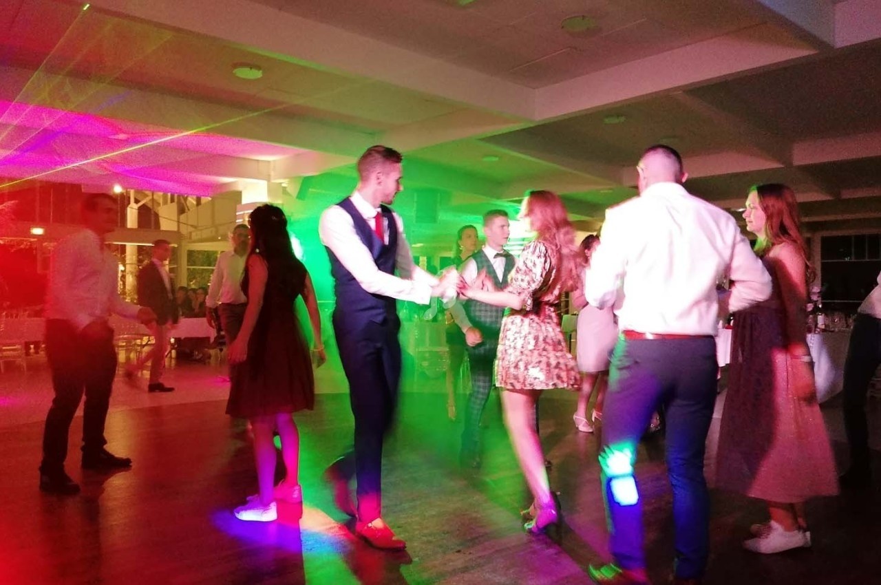 Des personnes dansent sous des lumières colorées dans une salle éclairée, ambiance festive et conviviale.
