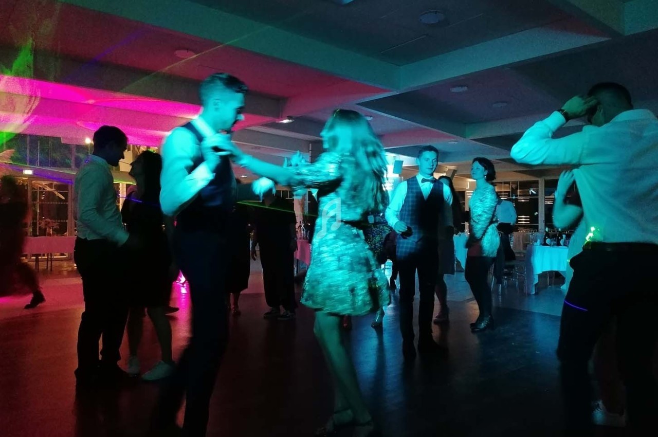 Des personnes dansent dans une salle éclairée par des lumières colorées lors d'une fête ou d'un événement.