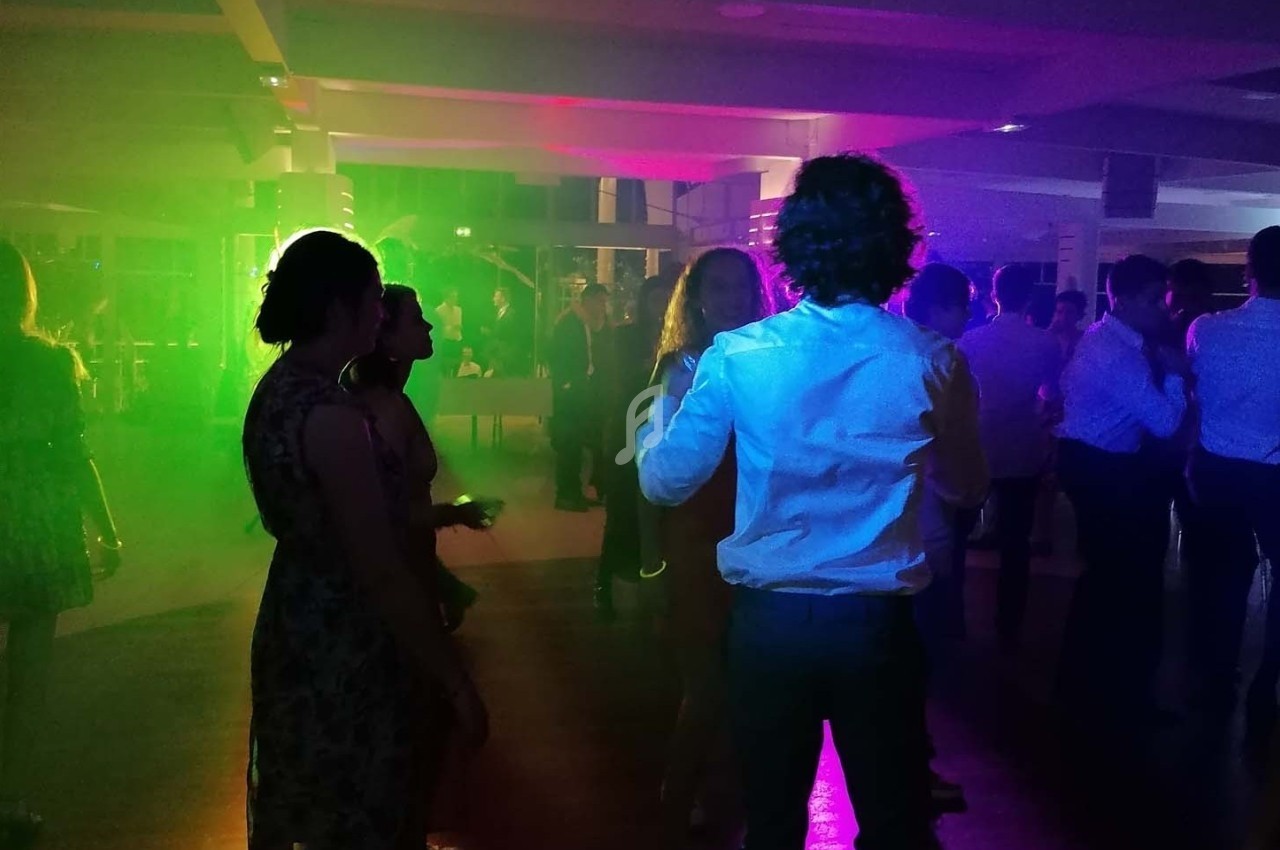 Personnes dansant dans une salle éclairée par des lumières colorées, ambiance festive en soirée.