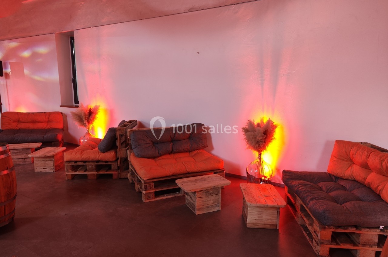 Canapés en palettes avec coussins orange, éclairés par une lumière chaude, disposés dans un espace intérieur minimaliste.