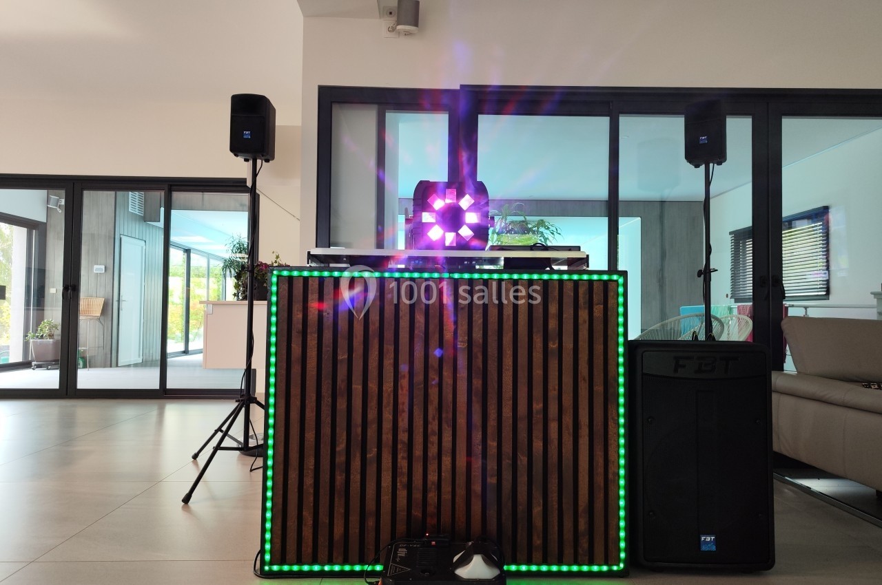 Console de DJ en bois éclairée par des lumières colorées, entourée de haut-parleurs dans une pièce moderne.
