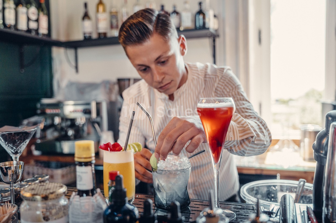 Un barman prépare des cocktails variés sur un comptoir dans un bar bien équipé.