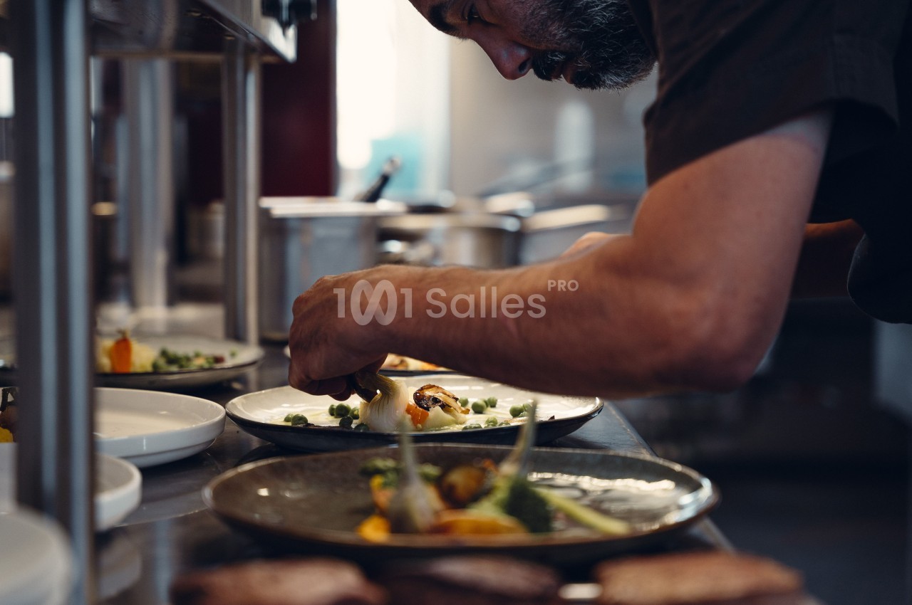 Un chef cuisine en dressant soigneusement des assiettes avec des légumes dans une cuisine professionnelle.