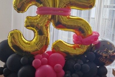 Arc décoratif en ballons roses, bleus et dorés avec papillons, installé dans une pièce au sol en bois.