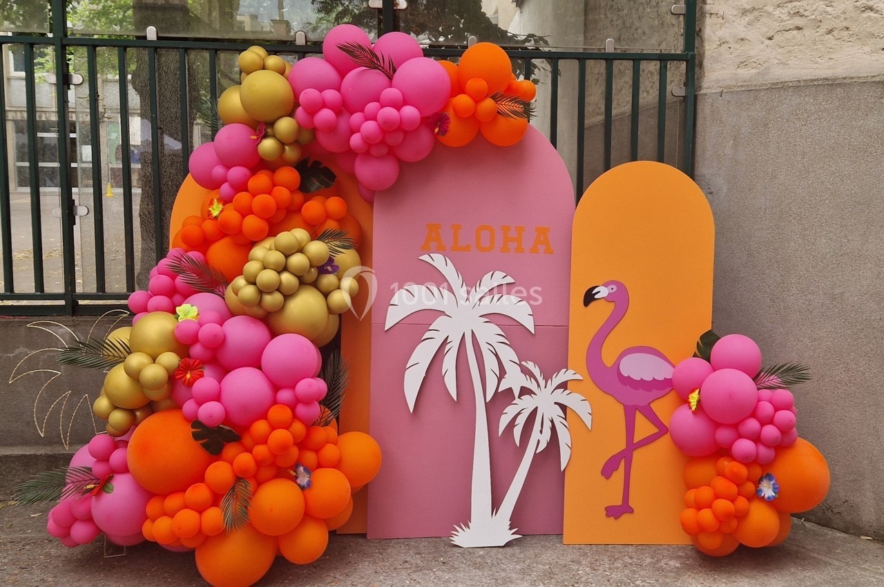 Décoration festive avec ballons colorés, silhouettes de palmier et flamant rose sur fond rose et orange.