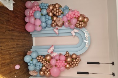 Arc décoratif en ballons roses, bleus et dorés avec papillons, installé dans une pièce au sol en bois.