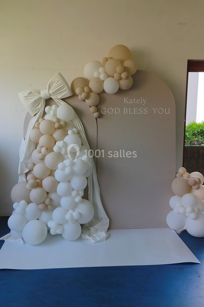 Décor avec arche beige ornée de ballons blancs et crème, ruban blanc et inscription ’God bless you’.