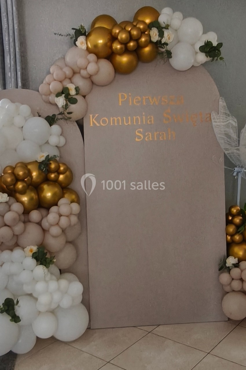 Décor de communion avec arche de ballons blancs, dorés et beiges, et panneau personnalisé avec un prénom.