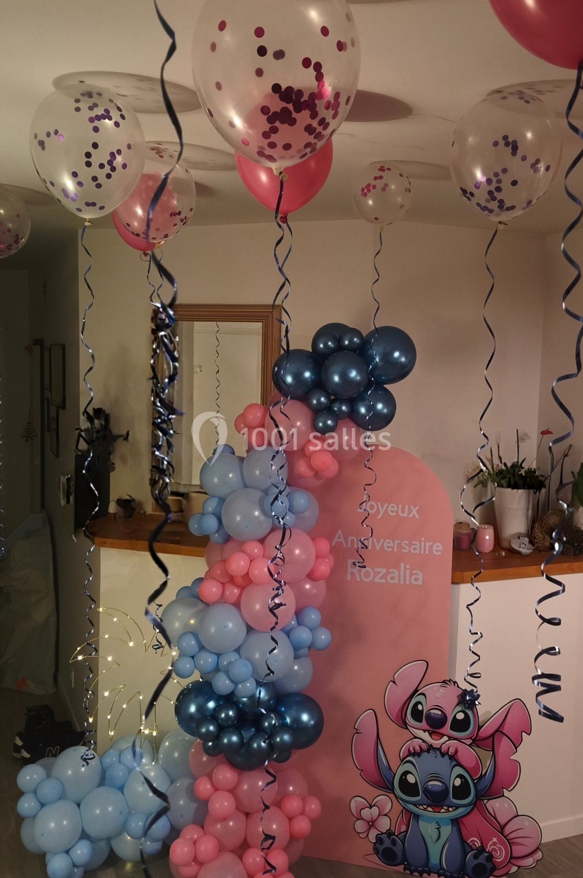 Décoration d'anniversaire avec ballons roses et bleus, affichage personnalisé et ballons suspendus dans une pièce.