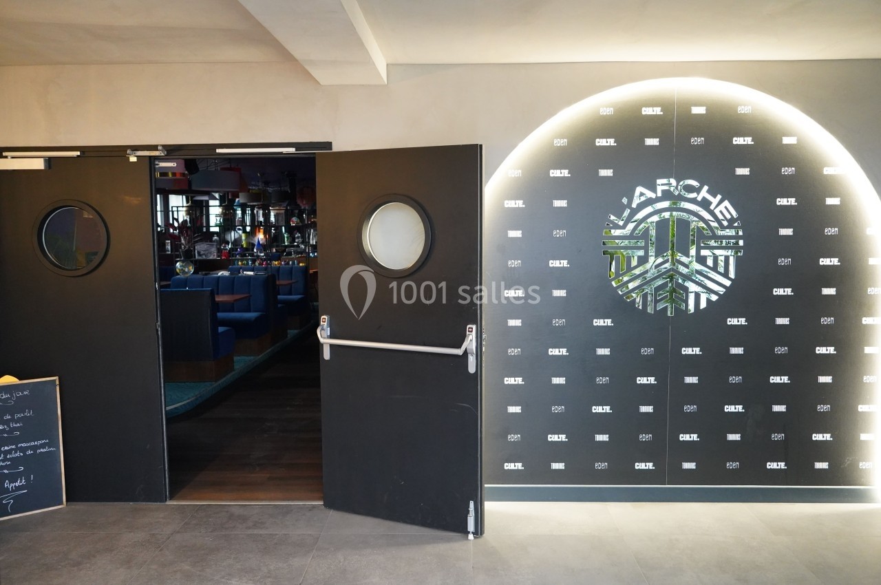 Entrée d'un restaurant avec portes battantes noires et mur décoratif éclairé affichant le logo ’Apache’.