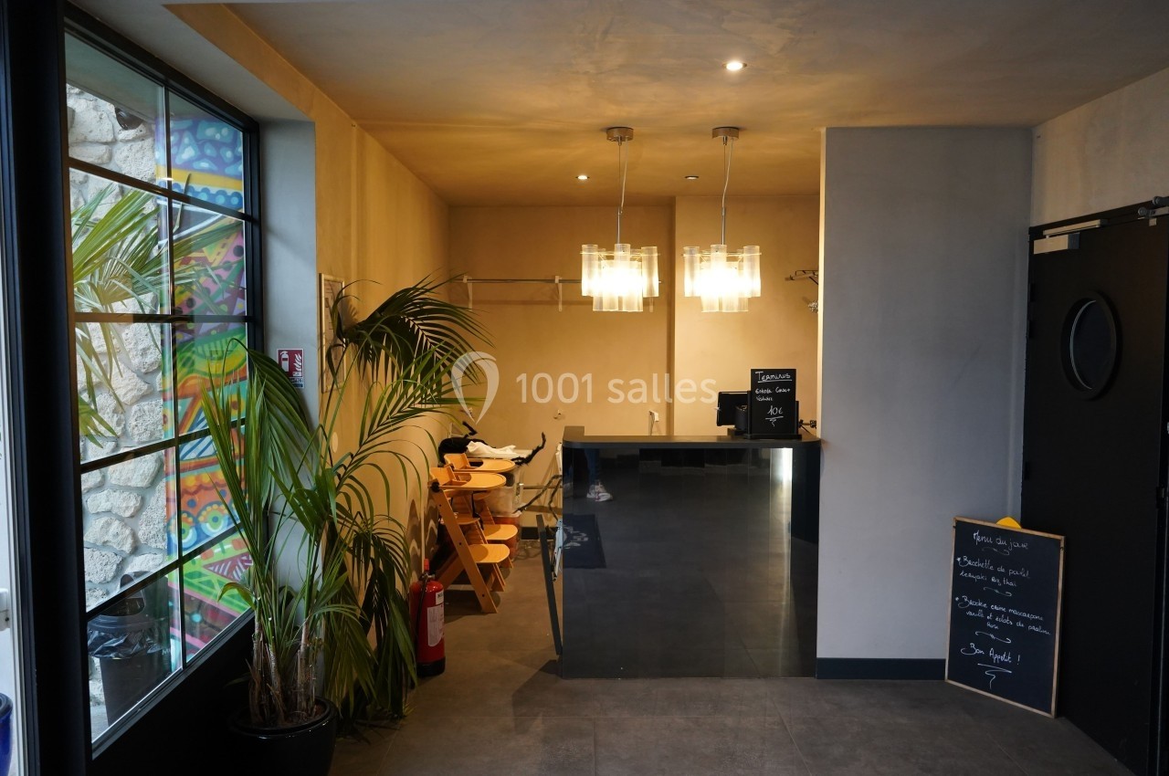 Vue d'un espace intérieur avec un comptoir moderne, des plantes, des chaises en bois et une ardoise d'informations.