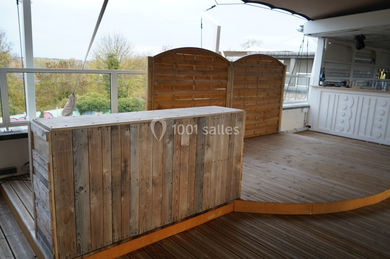Comptoir en bois brut sur une terrasse en bois avec des panneaux en arrière-plan et une vue extérieure dégagée.