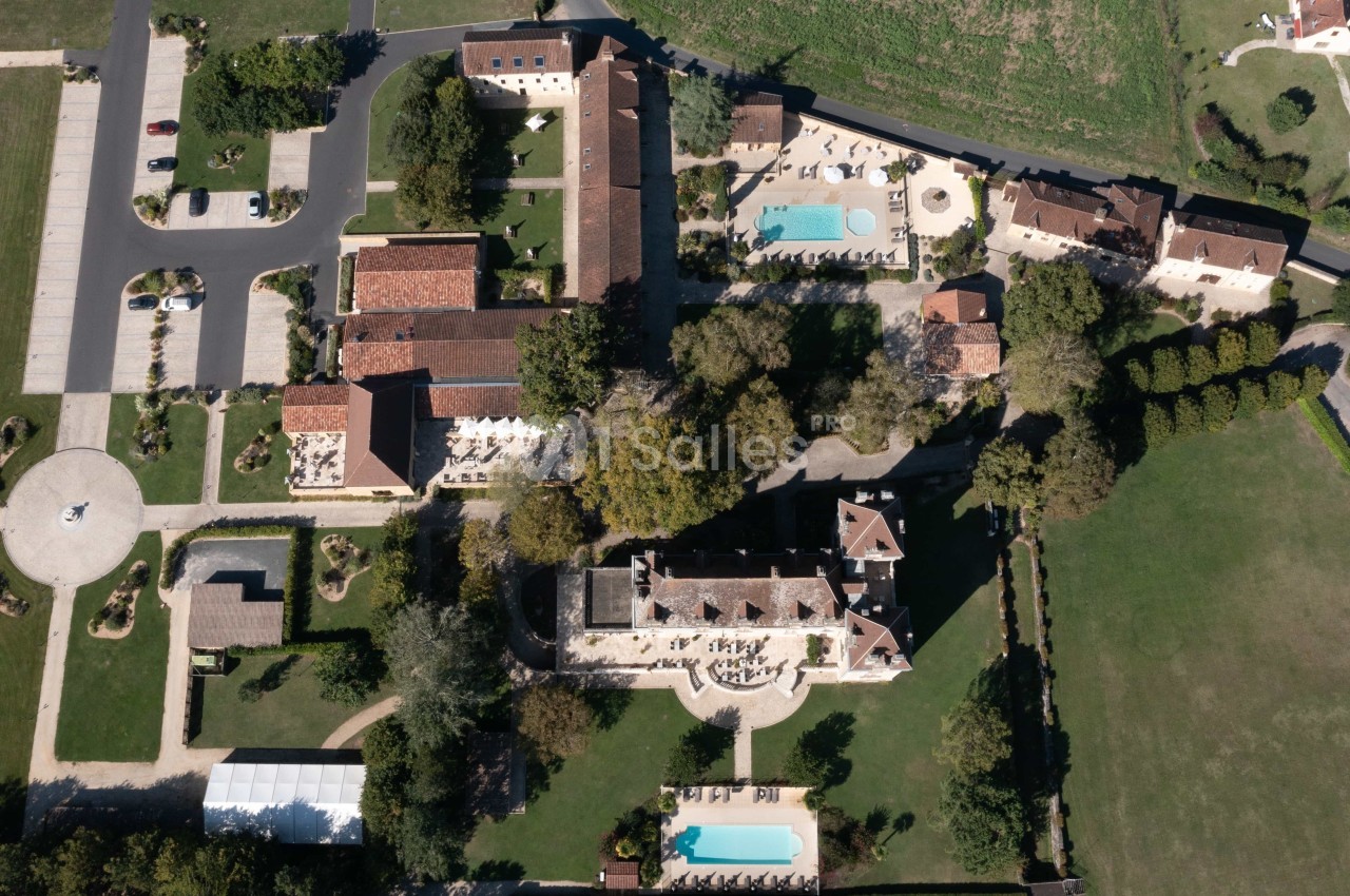 Vue aérienne d'un domaine avec bâtiments en pierre, piscines, espaces verts et allées aménagées.