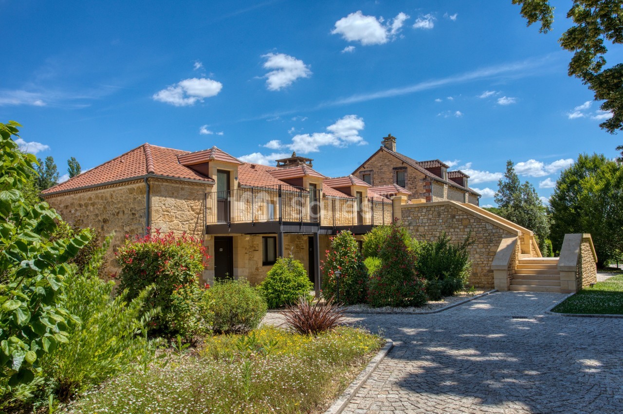 Bâtiment en pierre avec toit en tuiles rouges, entouré de végétation et accessible par un escalier extérieur.
