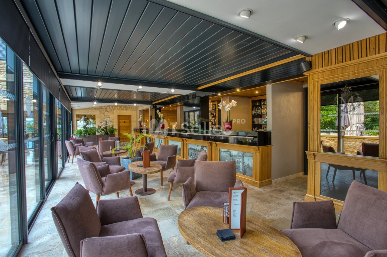 Espace lounge moderne avec fauteuils, tables basses, bar en bois et grandes baies vitrées donnant sur l'extérieur.