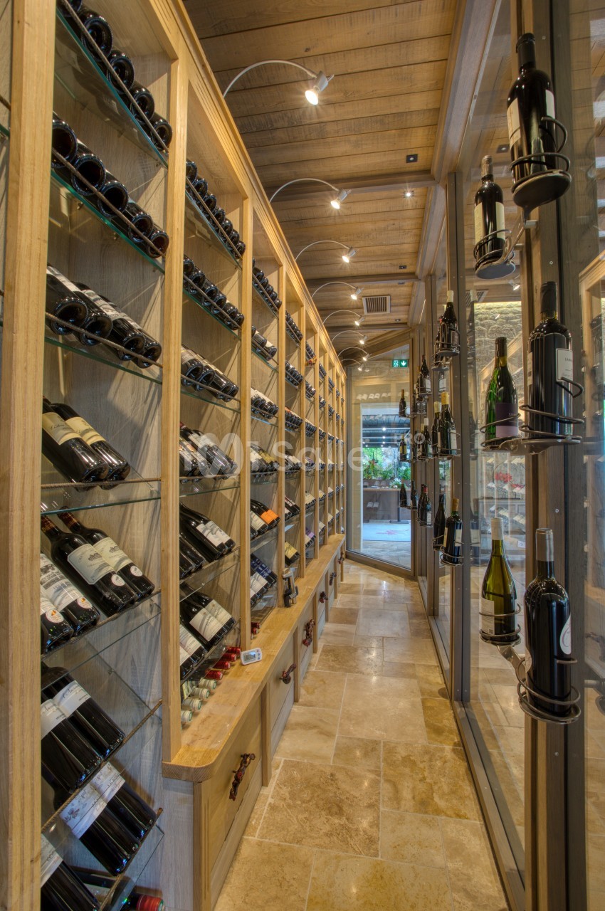 Cave à vin avec étagères en bois remplies de bouteilles, éclairage tamisé et sol en pierre beige.