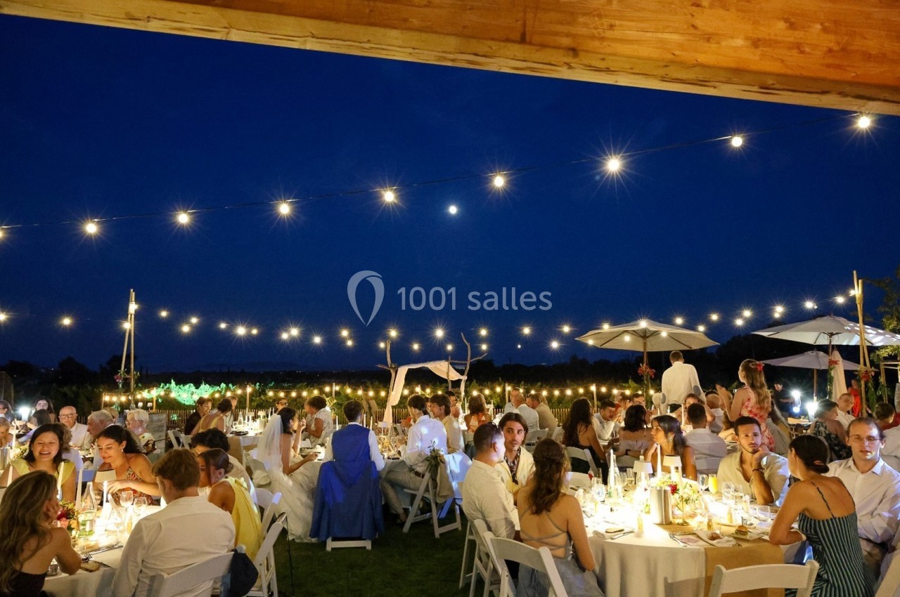 Des invités dînent en extérieur sous des guirlandes lumineuses, de nuit, dans une ambiance festive.