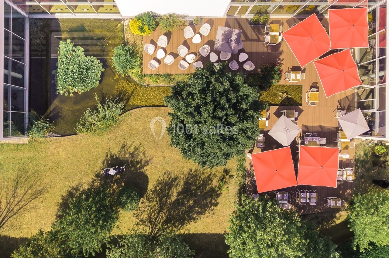 Vue aérienne d'une terrasse avec tables et parasols rouges entourée de verdure et d'un espace paysager.