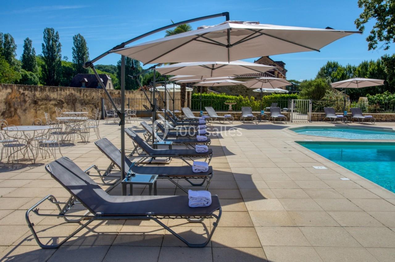 Chaises longues alignées avec serviettes sous des parasols près d'une piscine sur une terrasse ensoleillée.