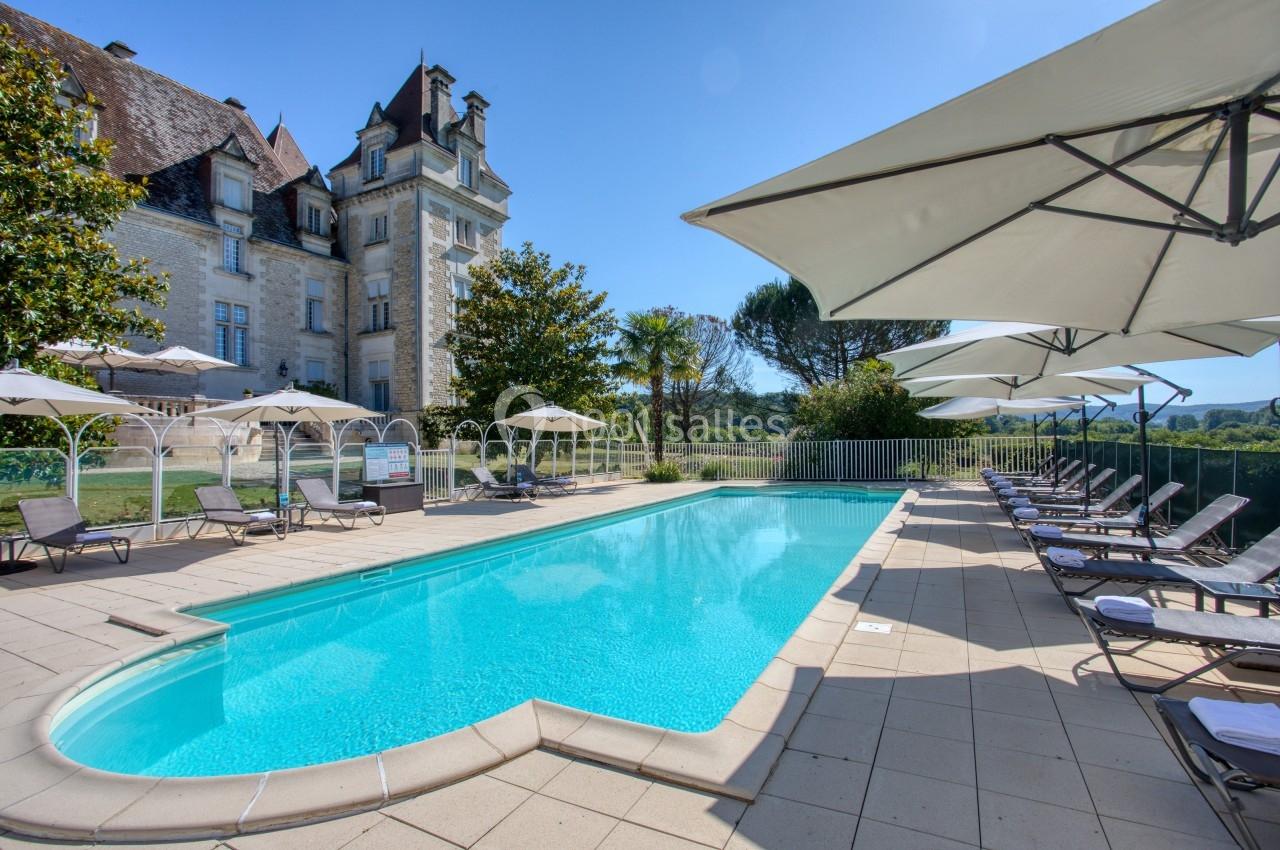 Piscine extérieure avec transats et parasols, située devant un bâtiment ancien entouré de verdure.