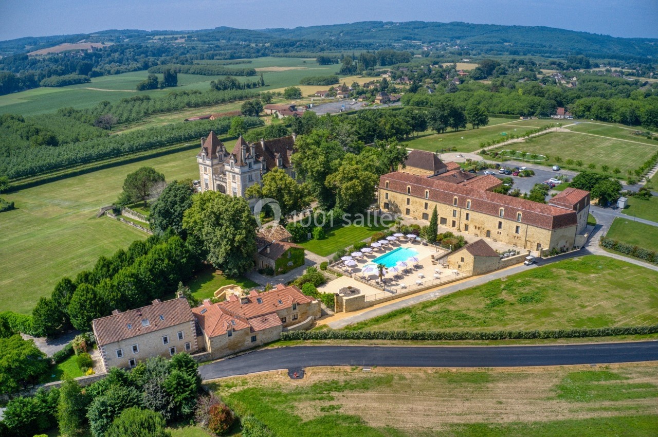 Vue aérienne d'un domaine avec un château, des bâtiments en pierre, une piscine et des champs environnants verdoyants.