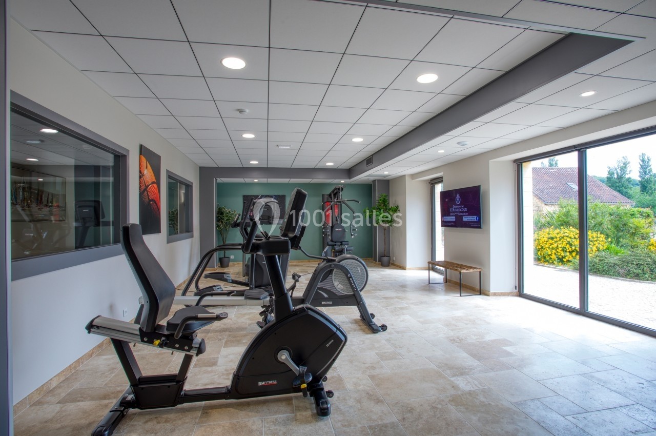 Salle de sport lumineuse avec vélos d'exercice, tapis de course et vue sur l'extérieur par une grande baie vitrée.