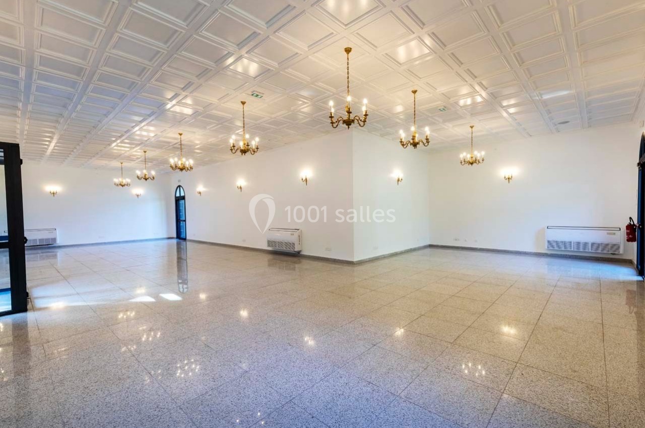 Salle spacieuse et lumineuse avec sol en carrelage, murs blancs, plafond à caissons et lustres suspendus.