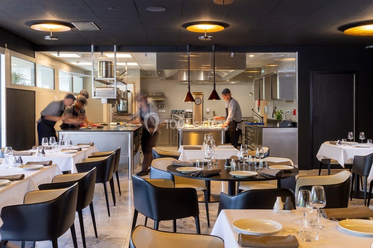 Cuisine ouverte d'un restaurant avec des chefs en action, tables dressées au premier plan.