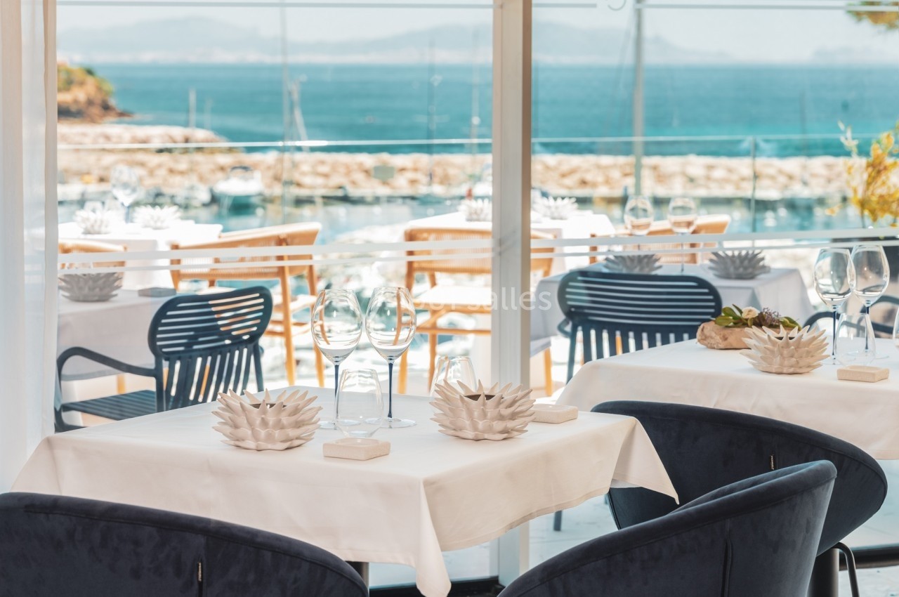 Salle de restaurant lumineuse avec vue sur la mer, tables dressées avec nappes blanches et décoration élégante.