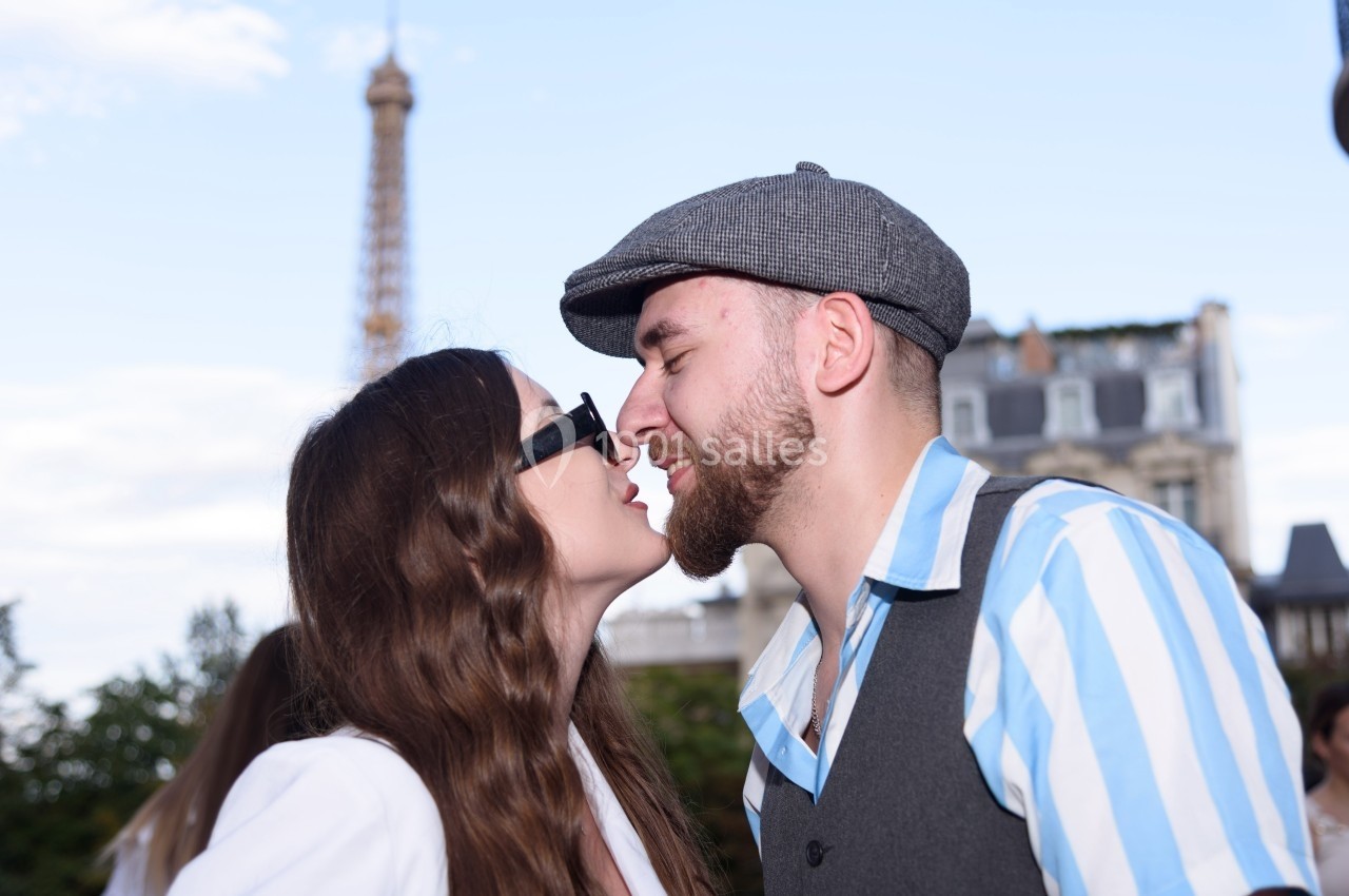 Un couple s'embrasse devant un paysage urbain avec la tour Eiffel visible en arrière-plan.