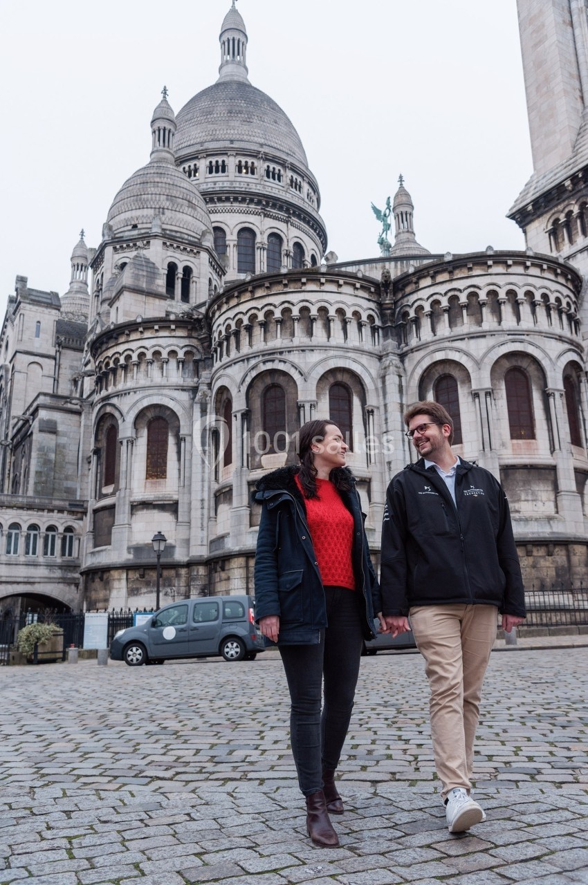 Un couple marche main dans la main devant la basilique du Sacré-Cœur à Paris par temps nuageux.