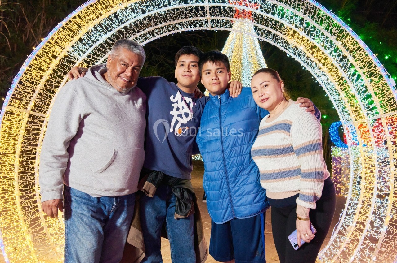 Une famille pose souriante devant une structure lumineuse en forme d'arche dans un décor nocturne festif.