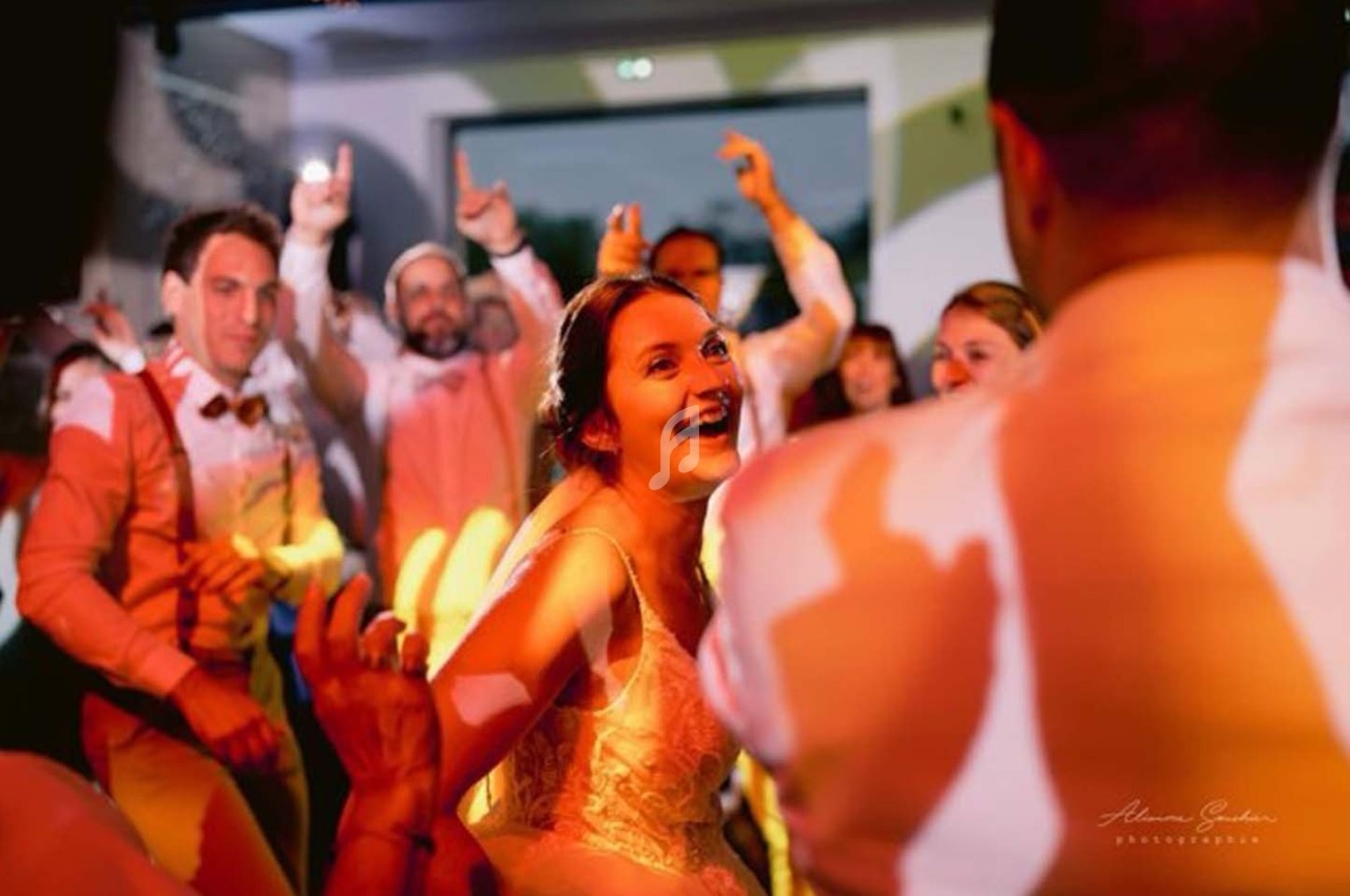 Une mariée souriante danse entourée d'invités lors d'une fête animée avec des lumières colorées.