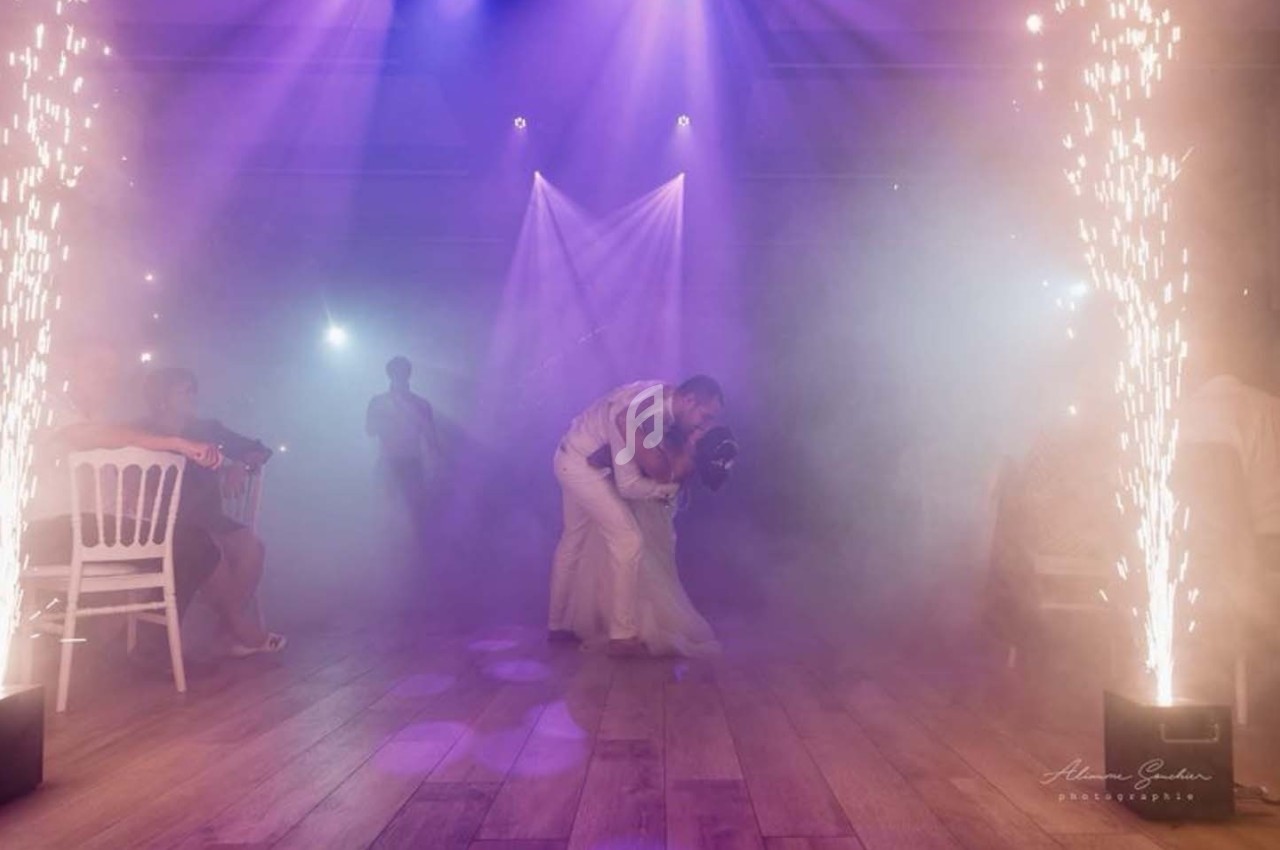 Un couple danse au centre d'une piste éclairée par des projecteurs violets et des étincelles, entouré de spectateurs.
