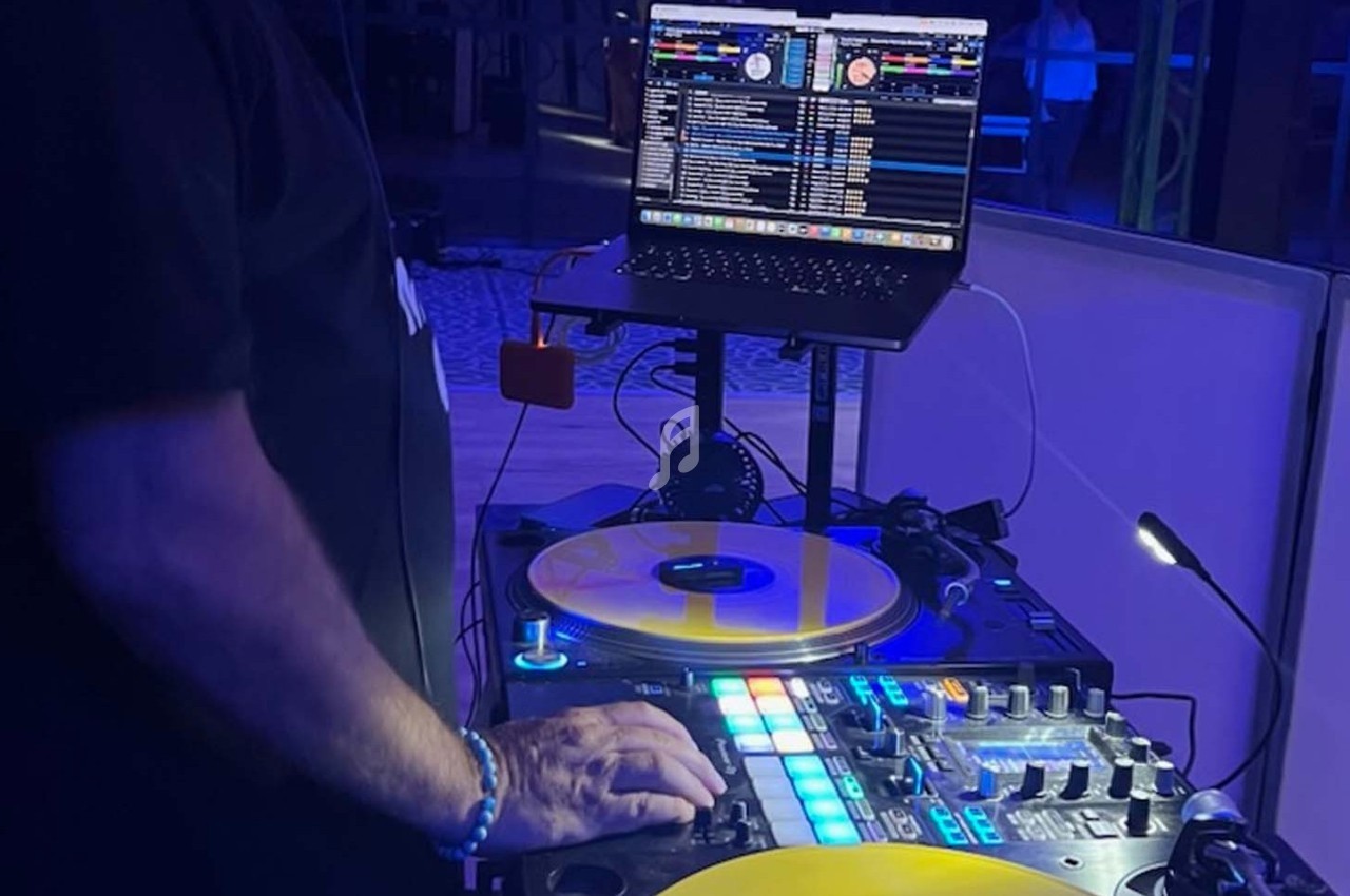 Un DJ mixant sur une table de mixage équipée de vinyles jaunes et d'un ordinateur portable affichant des playlists.
