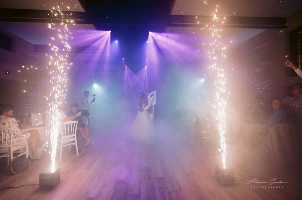 Un couple danse au centre d'une salle éclairée par des projecteurs violets, entouré de jets d'étincelles et de fumée.