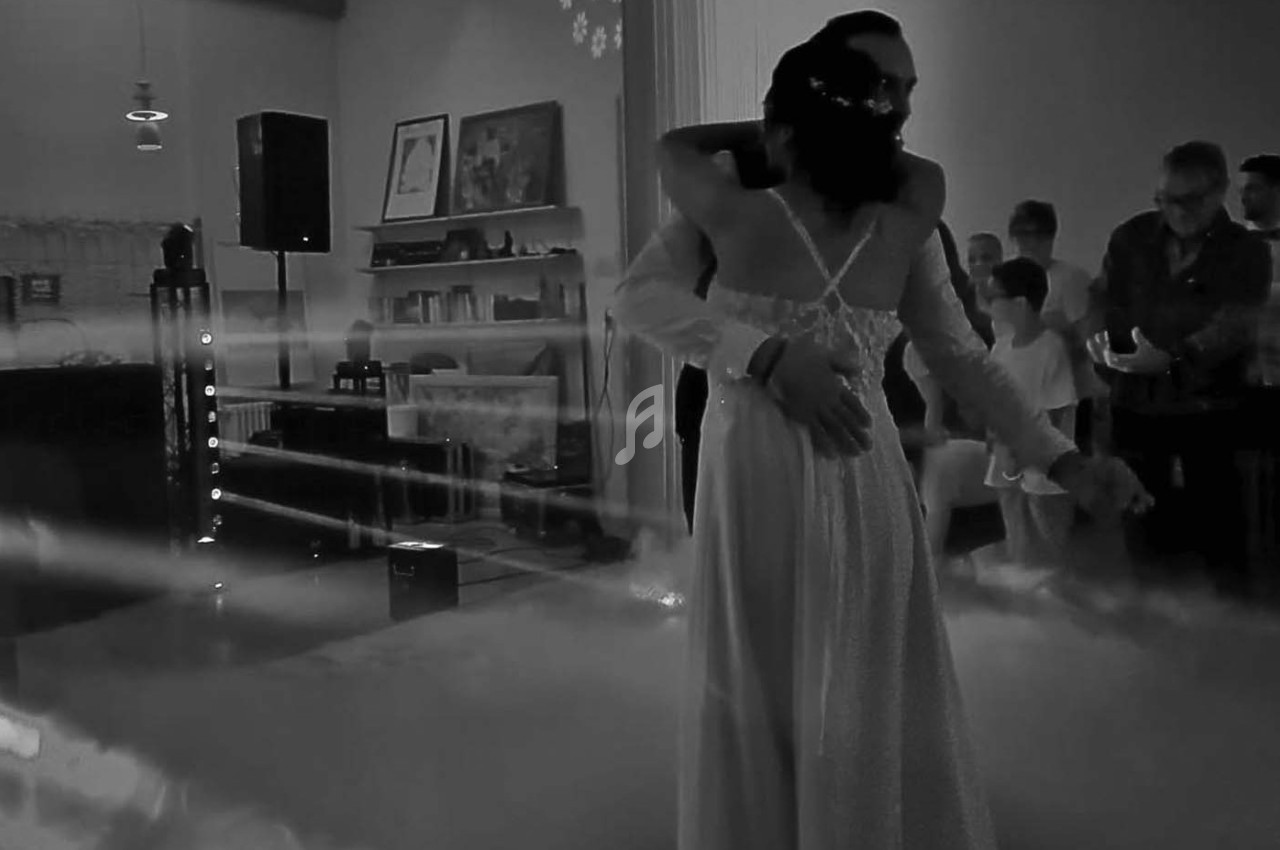 Un couple danse dans une salle éclairée de manière tamisée, entouré de spectateurs et d'une légère brume au sol.