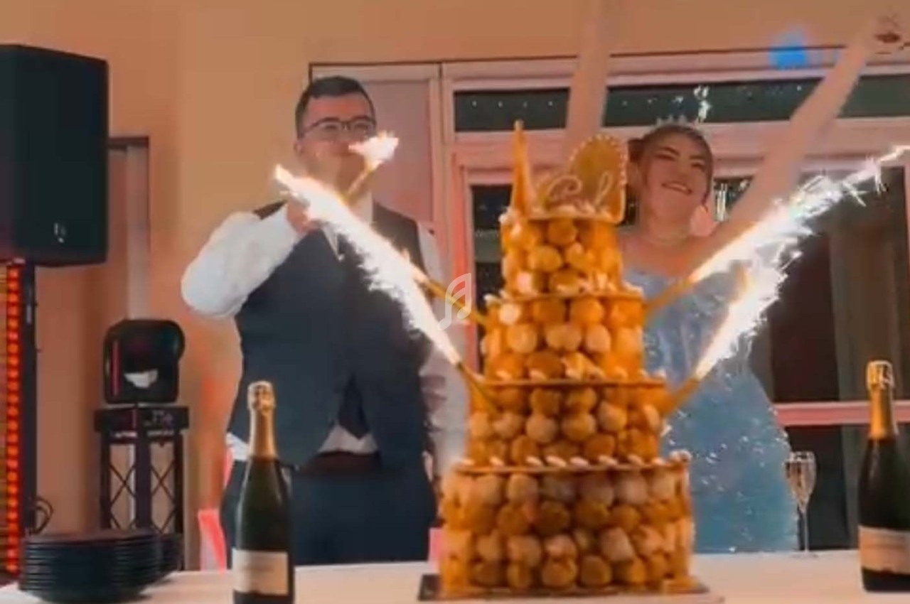 Un couple souriant près d'une pièce montée éclairée par des cierges magiques, avec des bouteilles de champagne sur la table.