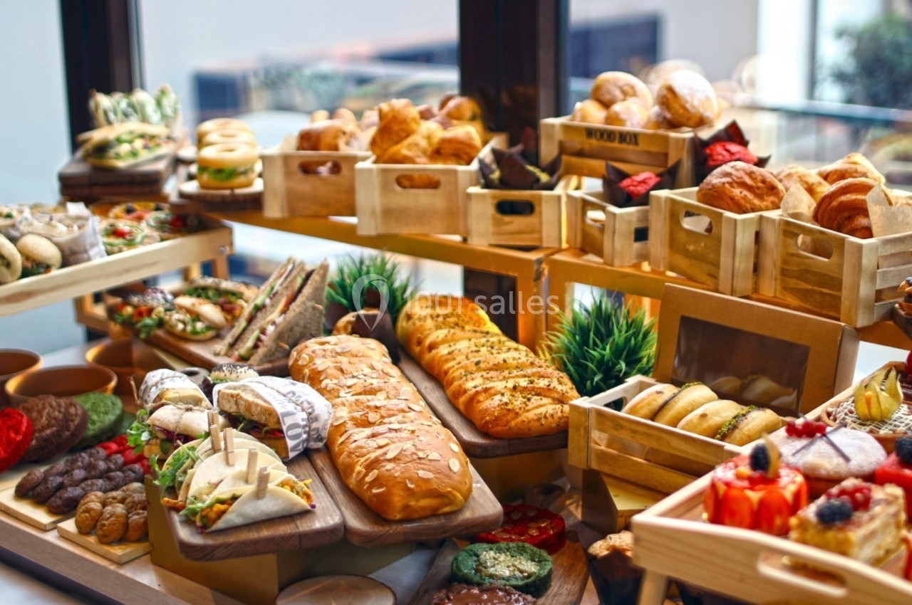 Table garnie de pains, viennoiseries, sandwichs et pâtisseries disposés dans des caisses en bois et sur des plateaux.
