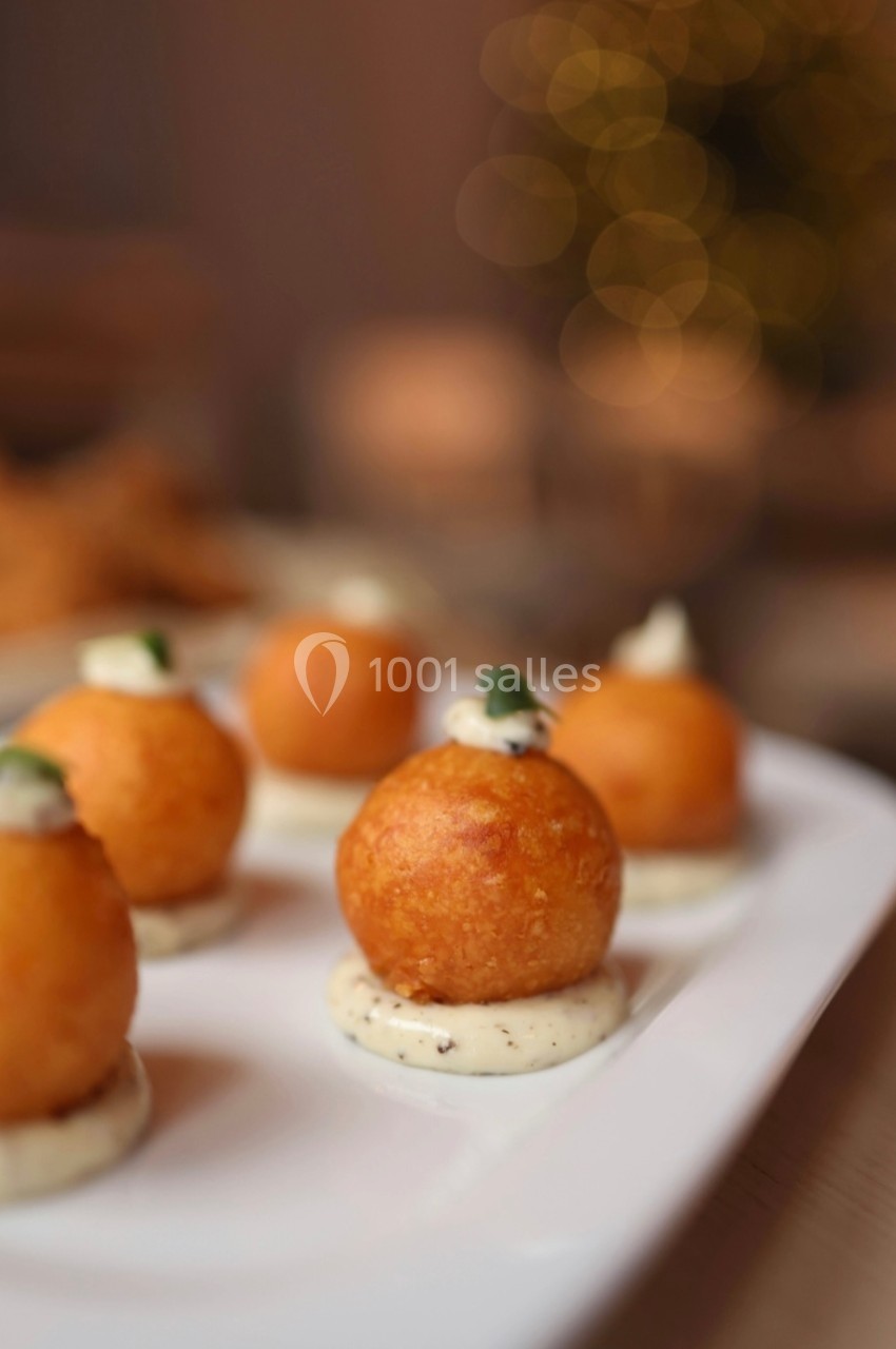 Bouchées apéritives dorées posées sur une sauce blanche, décorées d'une touche verte, servies sur une assiette blanche.